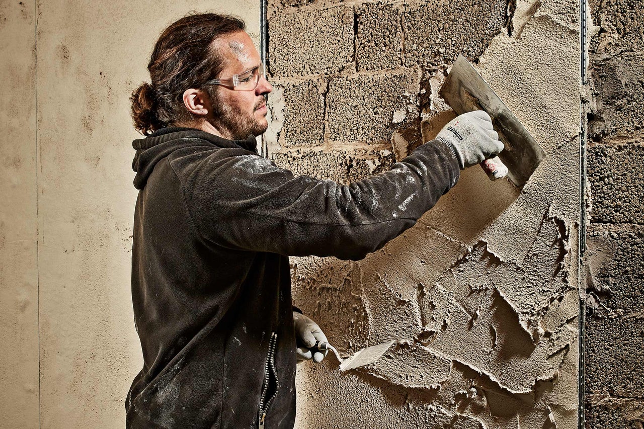 Handwerker trägt Putz mit einer Kelle auf eine Wand auf