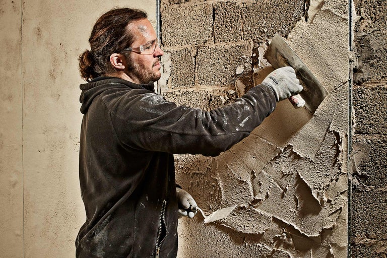 Handwerker trägt Putz mit einer Kelle auf eine Wand auf