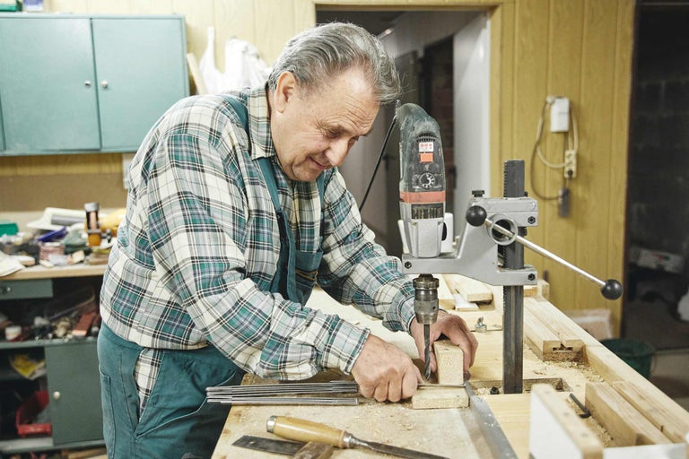 Mann bohrt Holz mit einer Standbohrmaschine in einer Werkstatt.