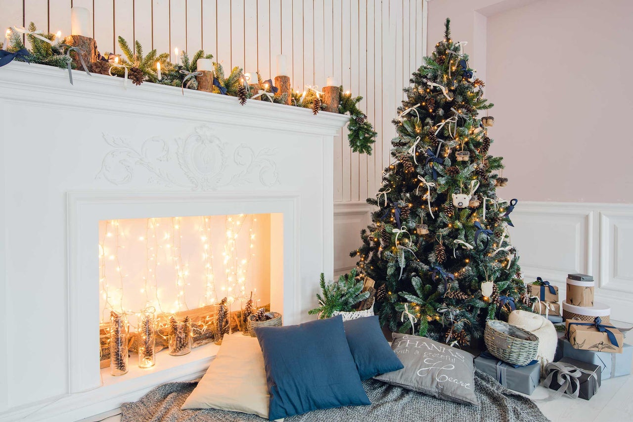 Dekorierter Weihnachtsbaum neben Kamin mit Dekoration und Geschenken