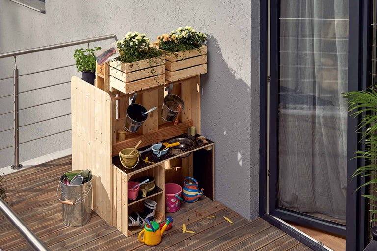 Holz-Matschküche mit Blumenkästen und Spielutensilien auf einer Terrasse