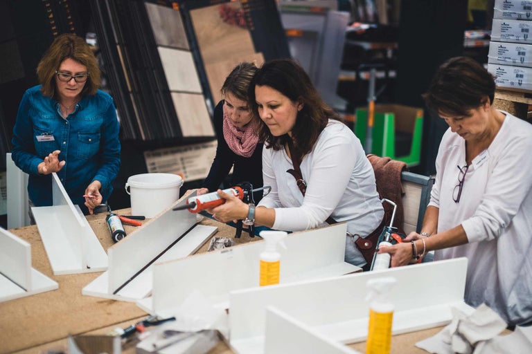 Frauen kleben weiße Regalböden mit einer Kartuschenpistole zusammen.