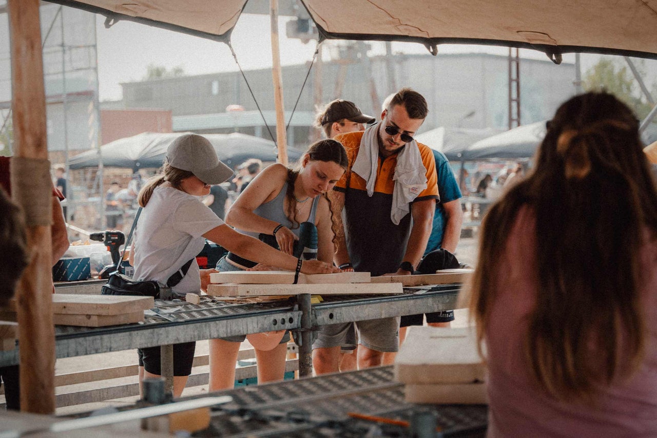 Personen arbeiten mit einem Akkuschrauber an Holz auf einem Metalltisch.