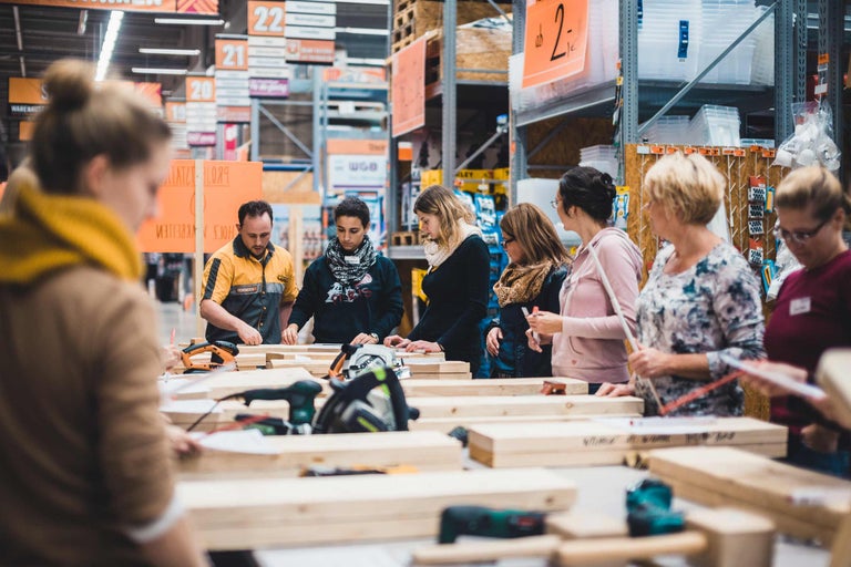 Personen arbeiten mit Holz und Elektrowerkzeugen in einem Baumarkt.