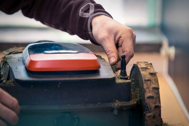 Ein Rasenmähroboter wird von einer Hand gereinigt.