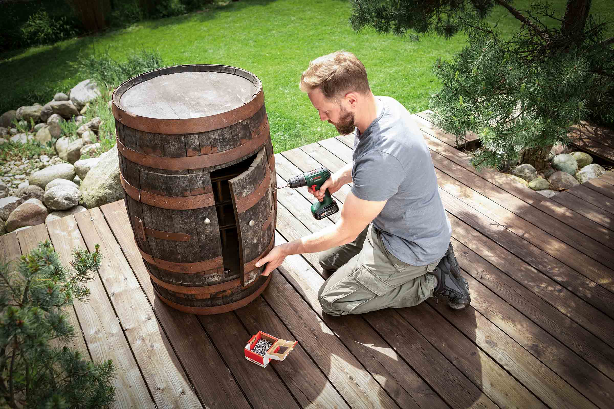 Mann montiert eine Bar aus einem Weinfass im Garten mit einem Akkuschrauber