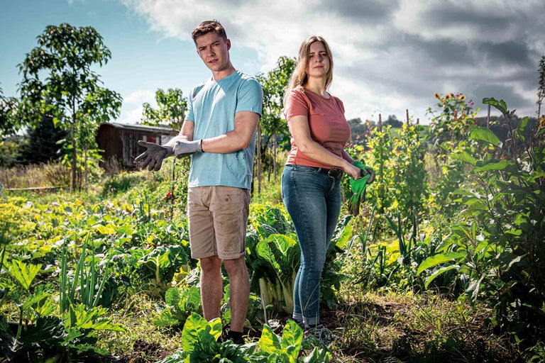 Ein Paar im Gemüsegarten mit Gartenhandschuhen und Gemüse.