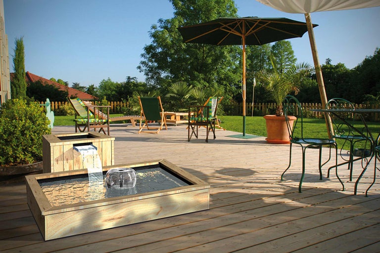 Garten Szene mit hölzernem Wasserspiel, Gartenmöbeln und Sonnenschirmen auf einer Holzterrasse