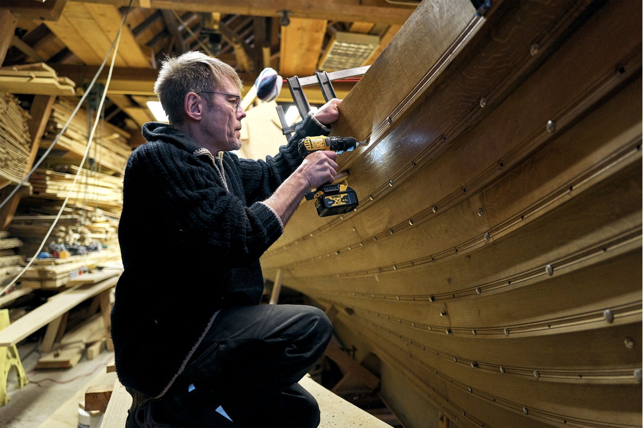 Mann arbeitet mit einem Akkubohrer an einem Holzboot
