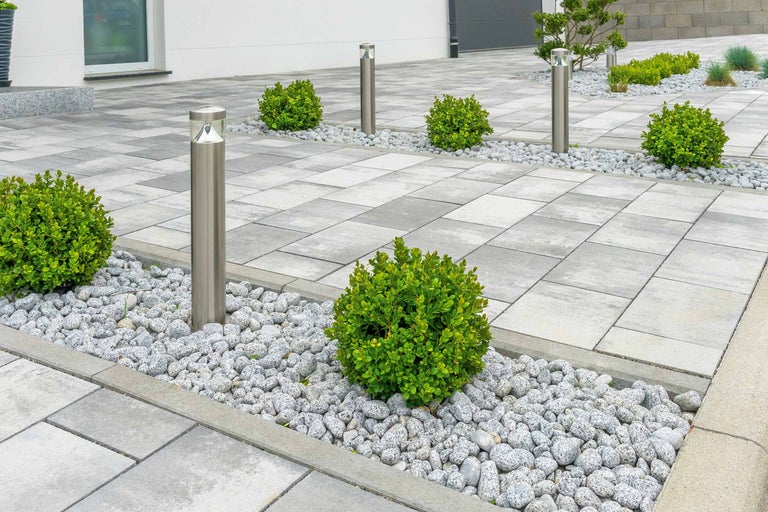 Außenbereich mit Betonpflastersteinen, Zierkies, Buchsbaumkugeln und Edelstahlleuchten