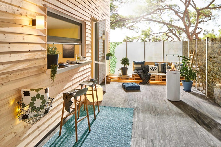Helle Terrasse mit Holzverkleidung, Barhockern, Teppich, Sitzgelegenheit aus Paletten und Außenkamin