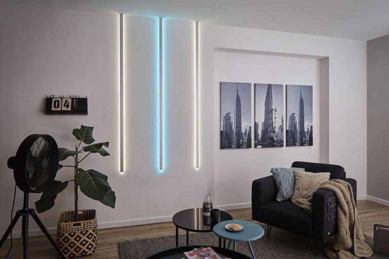Wohnzimmer mit Wandleuchten, Sessel, Tischen, Zimmerpflanze und Ventilator