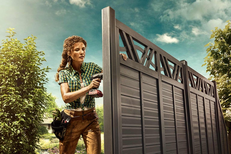 Frau montiert einen Sichtschutzzaun mit einem Akkuschrauber im Garten.