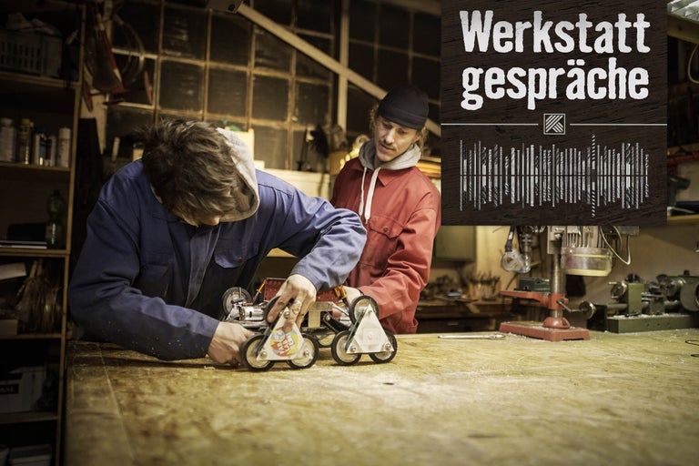 Zwei Personen arbeiten an einem Projekt in einer Werkstatt. Im Vordergrund ist der Titel Werkstattgespräche zu sehen.