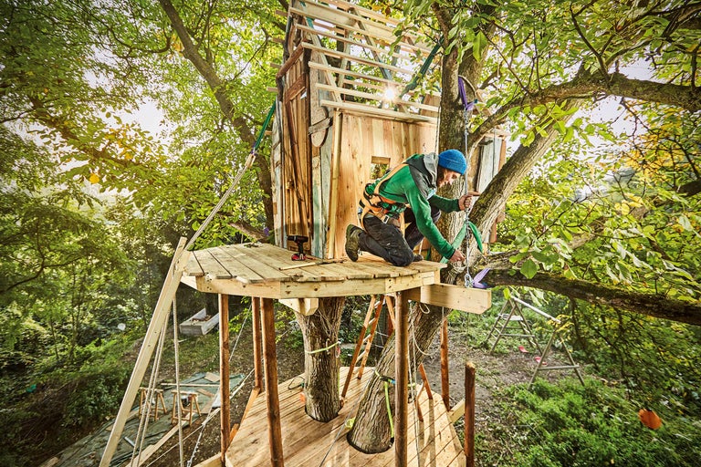 Mann baut Baumhaus mit Holzkonstruktion im Garten.