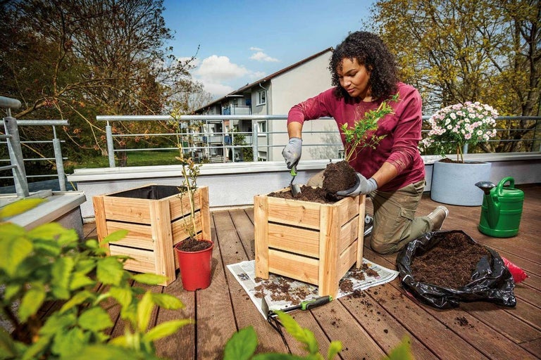 Frau pflanzt Pflanze in Holzkasten auf einer Terrasse mit Gartenzubehör