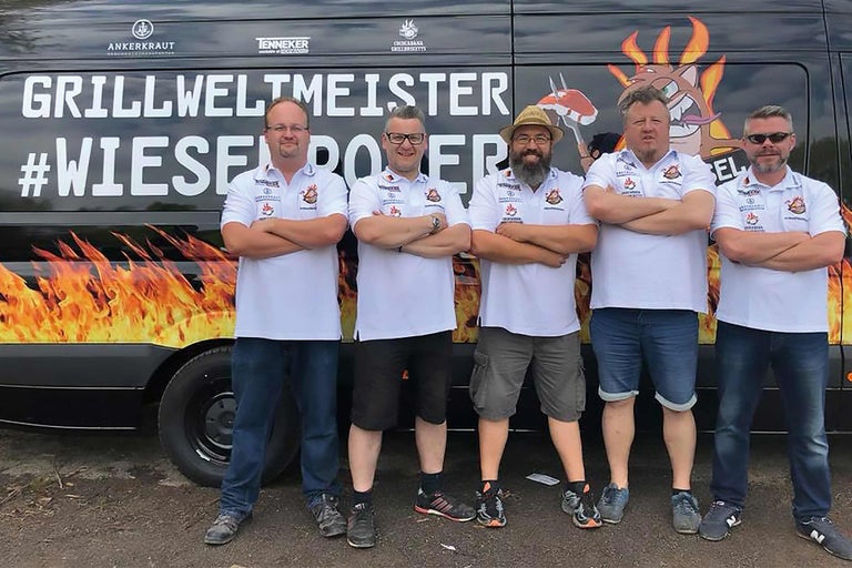 Fünf Personen vor einem Grillweltmeister-Bus mit Flammen-Design