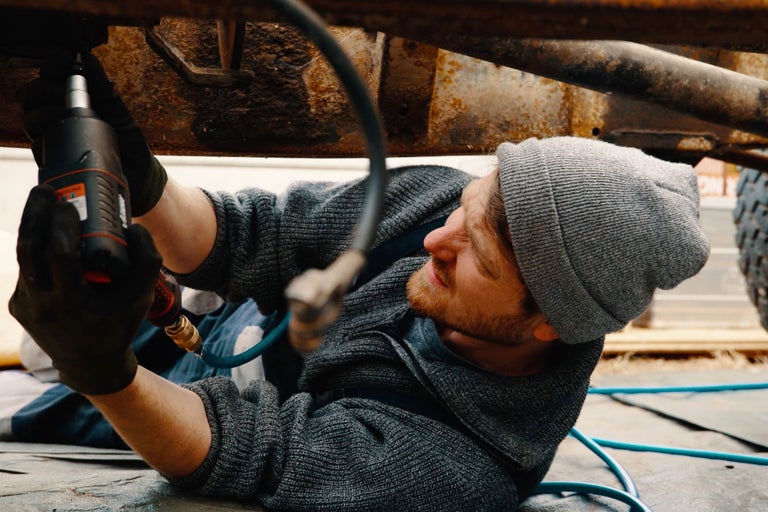 Mann benutzt einen Schlagschrauber, um an einem Auto zu arbeiten