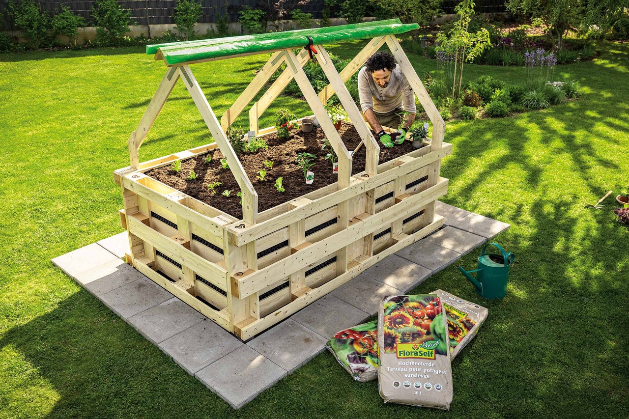 Hochbeet mit Frühbeetaufsatz und einer Person, die darin Pflanzen setzt, im Garten