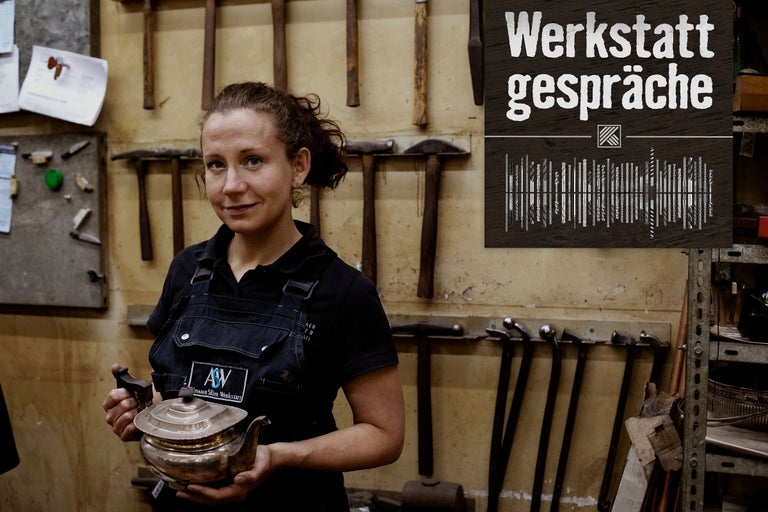 Eine Frau hält eine Teekanne in einer Werkstatt; im Hintergrund der Text Werkstattgespräche.
