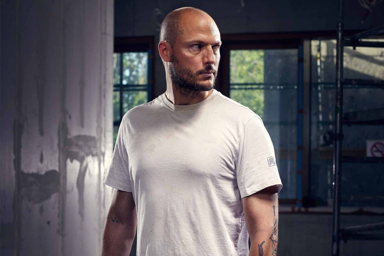 Mann mit Tätowierungen und kurzem T-Shirt im Rohbau