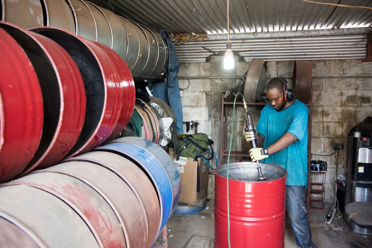 Mann mit Kopfhörern, der einen Farbmischer in einem Metallfass in einer Werkstatt verwendet