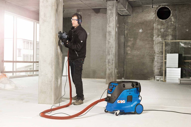 Ein Mann arbeitet mit einer Mauernutfräse und einem zugehörigen Industriesauger auf einer Baustelle.