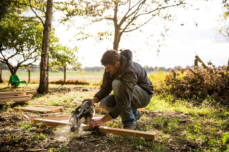 Handwerker schneidet Holzbrett mit einer Kreissäge im Garten.