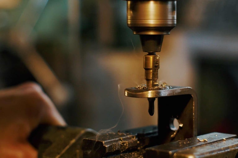 Metallbohrer bohrt durch ein Metallstück in einem Schraubstock.