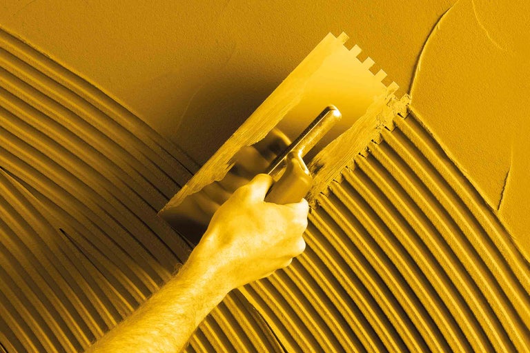 Handwerker trägt Klebstoff mit einer Zahnspachtel auf