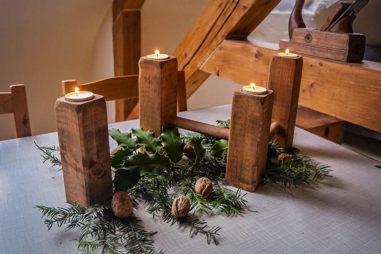 Adventskranz mit vier Teelichtern, Tannenzweigen, Walnüssen und Stechpalmenblättern auf einem Tisch