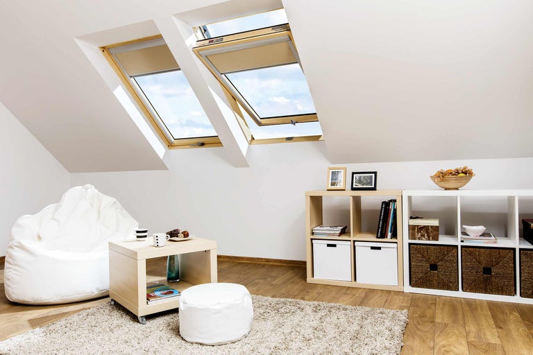 Helles Dachzimmer mit Dachfenstern und Rollos, Regalen und Sitzmöbeln.