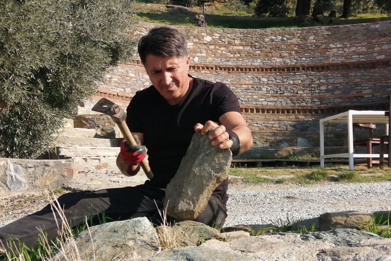 Mann bearbeitet Stein mit einem Hammer im Außenbereich.