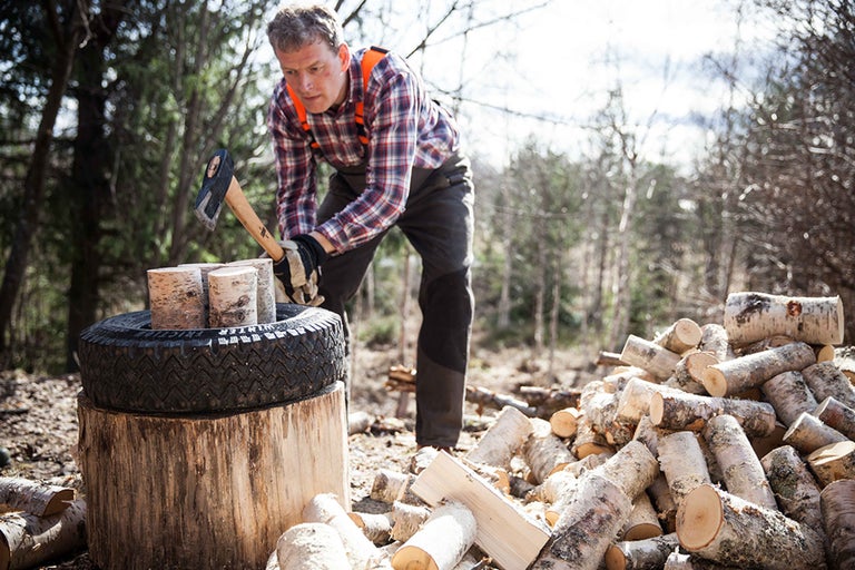 Mann spaltet Holz mit einer Axt im Freien