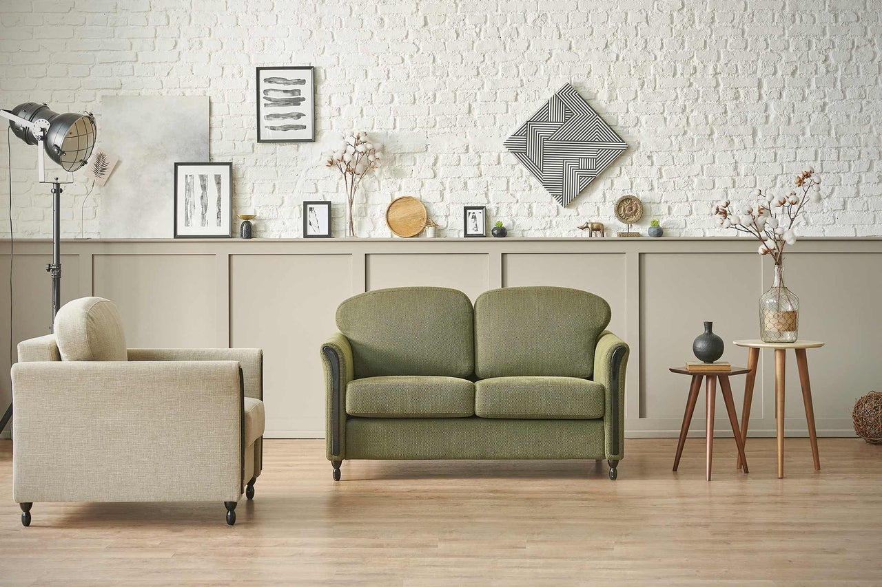 Wohnzimmer mit grüner Couch, Sessel und Dekoration vor einer weißen Ziegelwand