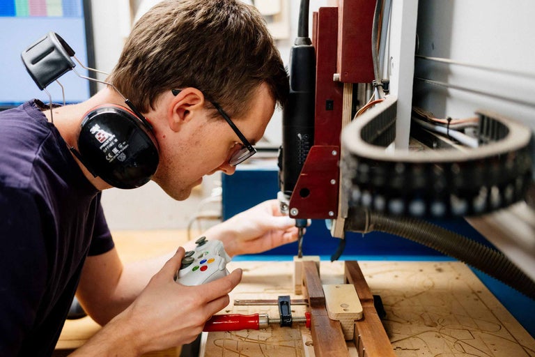 Ein Mann mit Kopfhörern und Brille bedient eine CNC-Fräse mit einem Gamecontroller.