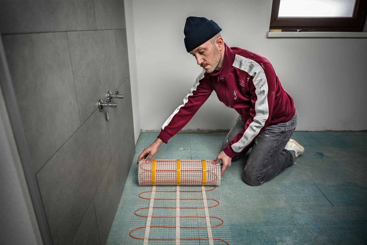 Ein Mann verlegt eine elektrische Fußbodenheizung.