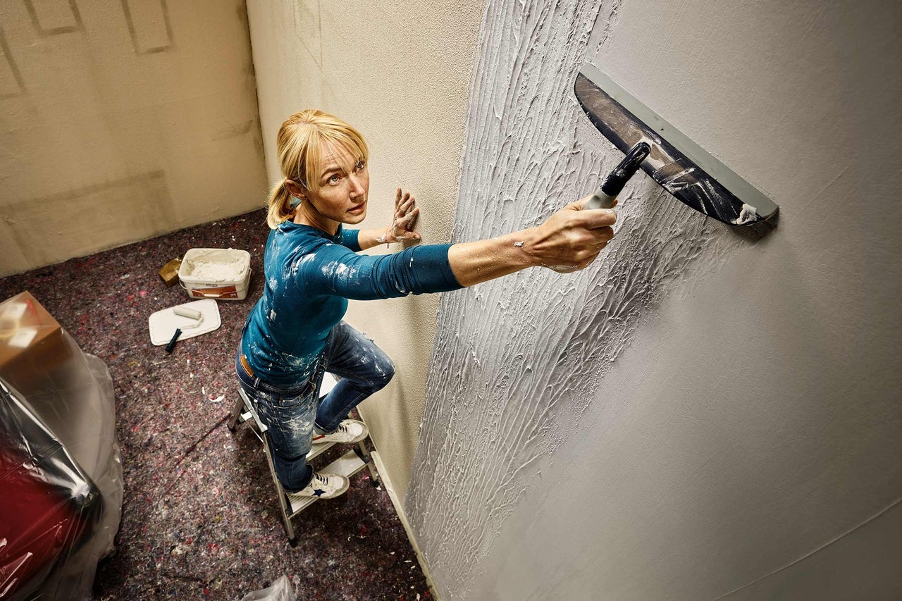 Frau auf einer Leiter, die mit einer Venezianischen Glättkelle eine Wand verputzt