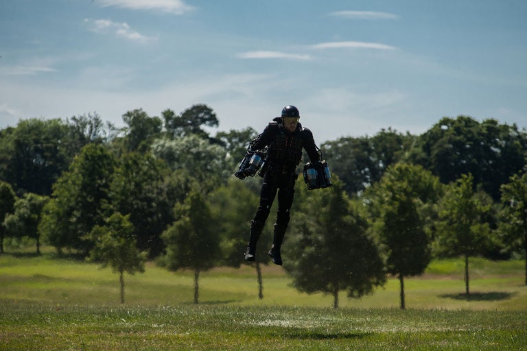 Eine Person fliegt mit einem Jetpack über eine grüne Wiese vor einem Hintergrund von Bäumen