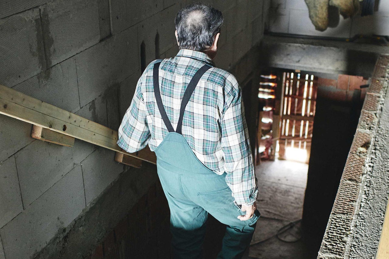 Mann mit Trägerhose und Holz auf einer Baustelle.