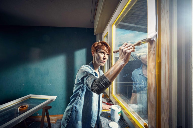 Eine Person streicht einen Fensterrahmen mit Pinsel und Farbe.
