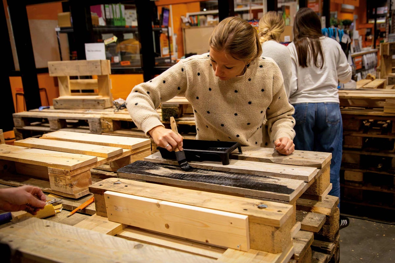 Eine Person streicht Holz mit einem Pinsel in einer Werkstatt.