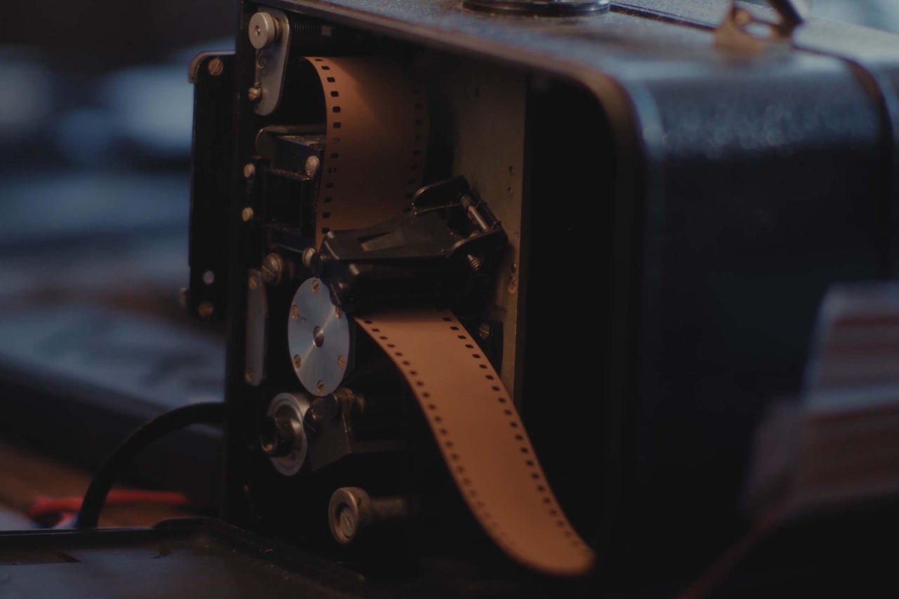 Nahaufnahme eines analogen Filmprojektors mit eingelegtem Filmstreifen im Inneren des geöffneten Gehäuses.