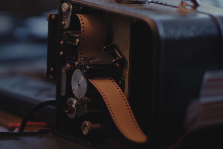 Nahaufnahme eines analogen Filmprojektors mit eingelegtem Filmstreifen im Inneren des geöffneten Gehäuses.