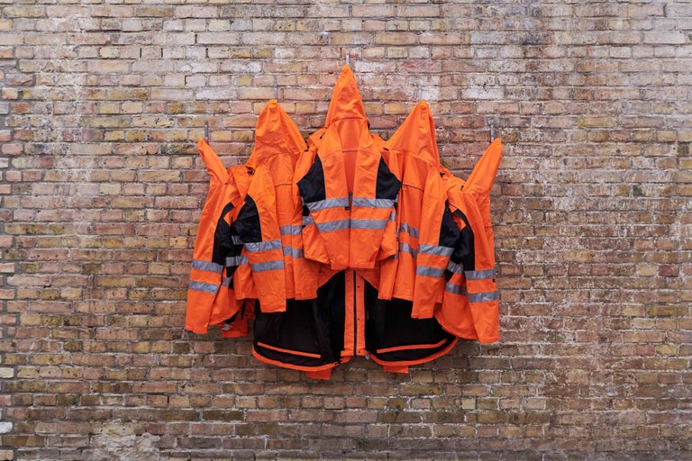 Mehrere Warnschutzjacken hängen an einer Backsteinmauer.
