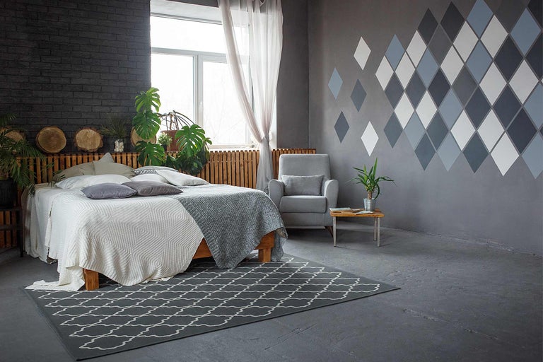 Helles Schlafzimmer mit Doppelbett, Sessel, kleinem Tisch und Teppich