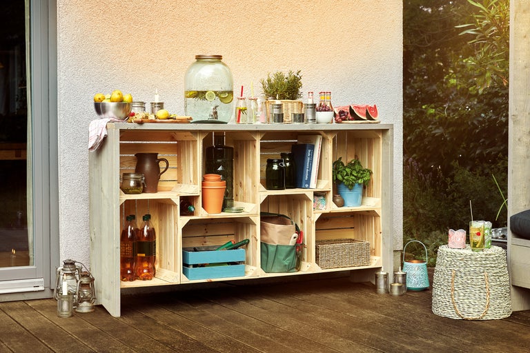 Outdoor-Szene mit einem Regal aus Holzkisten, dekoriert mit Getränken, Obst und Pflanzen