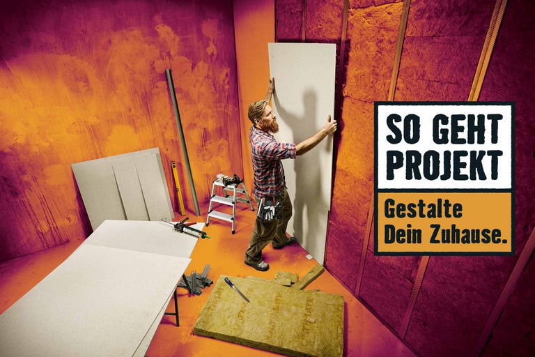 Ein Mann montiert eine Gipskartonplatte an einer Wand mit Dämmmaterial in einem Raum.