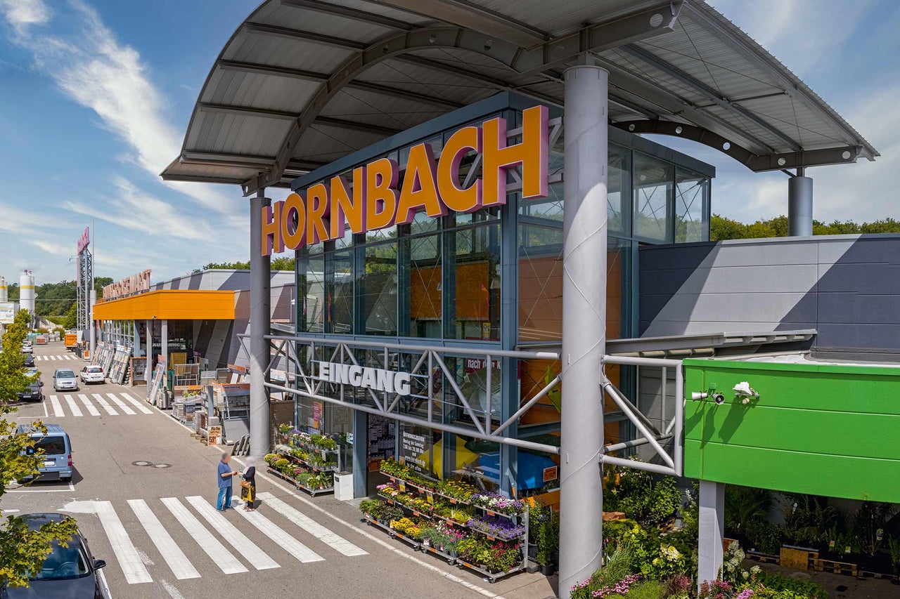  Außenansicht eines Hornbach Baumarktes mit Eingangsbereich und Pflanzen im Außenbereich. 