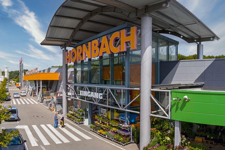 Außenansicht eines Hornbach Baumarktes mit Eingangsbereich und Pflanzen im Außenbereich.